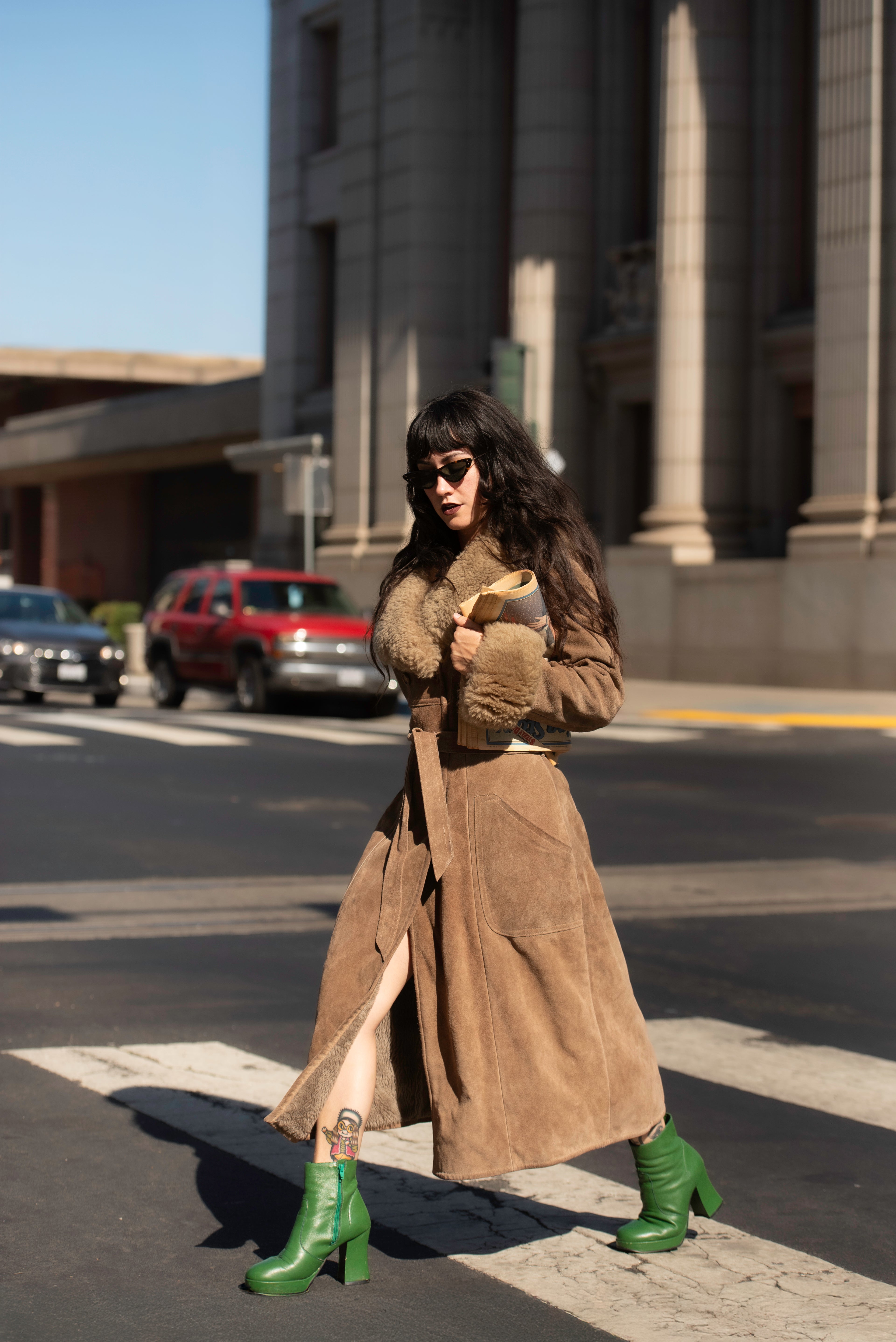 Woman in a long brown vintage coat with fur trim crossing a street.